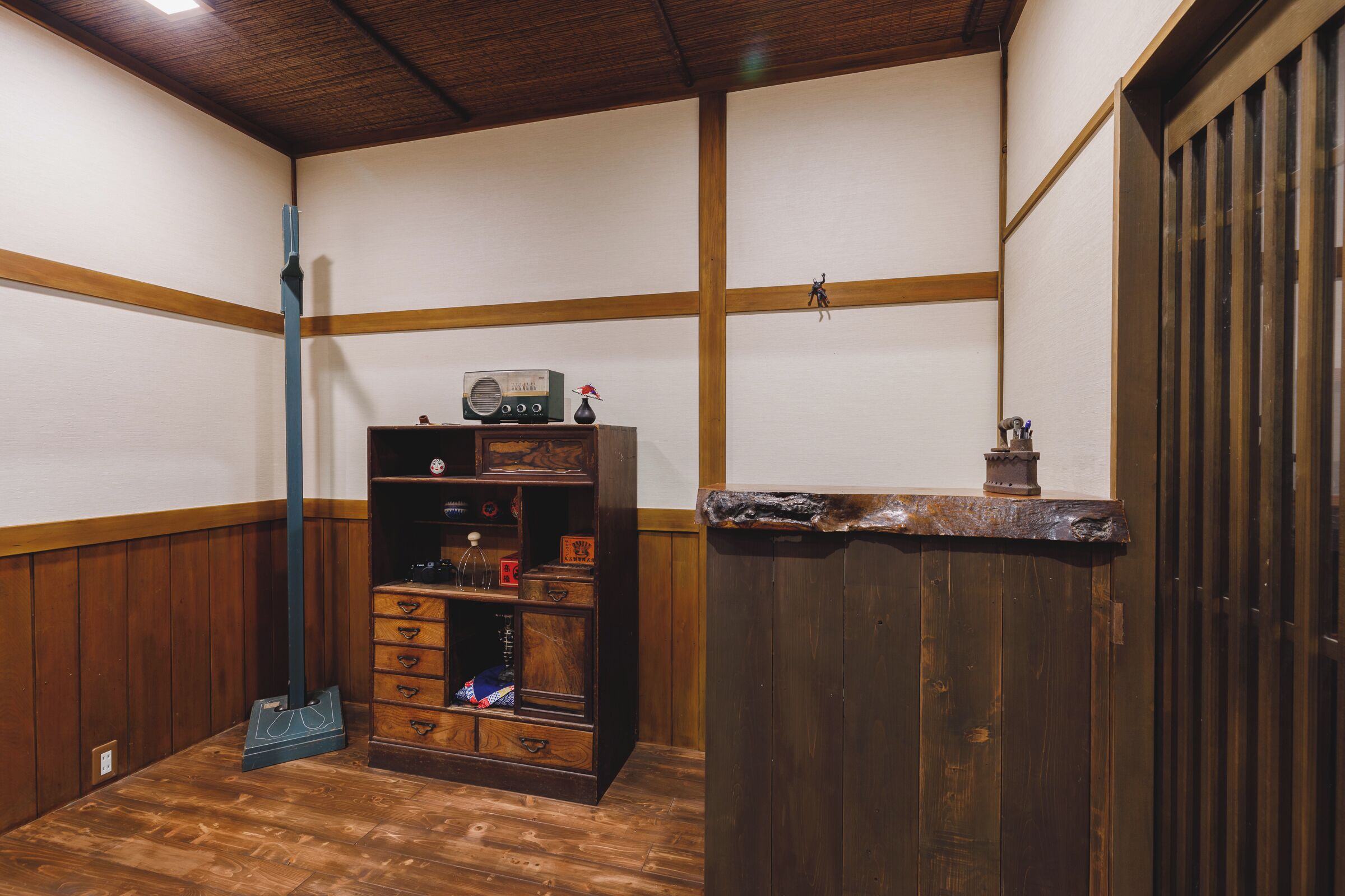 Une pièce aux murs et au plancher en bois, un meuble en bois avec des tiroirs, une radio et une petite statue posée sur une étagère.