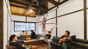 A cozy living room with wooden floors, a hammock, and a person playing guitar. - Couch Potato Hostel (Matsumoto)