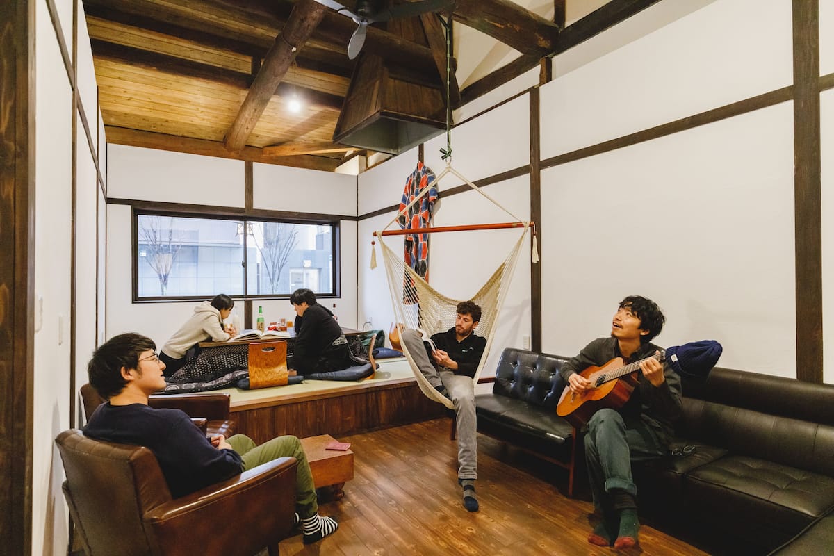 Ein gemütliches Wohnzimmer mit Holzböden, einer Hängematte und einer Person, die Gitarre spielt.