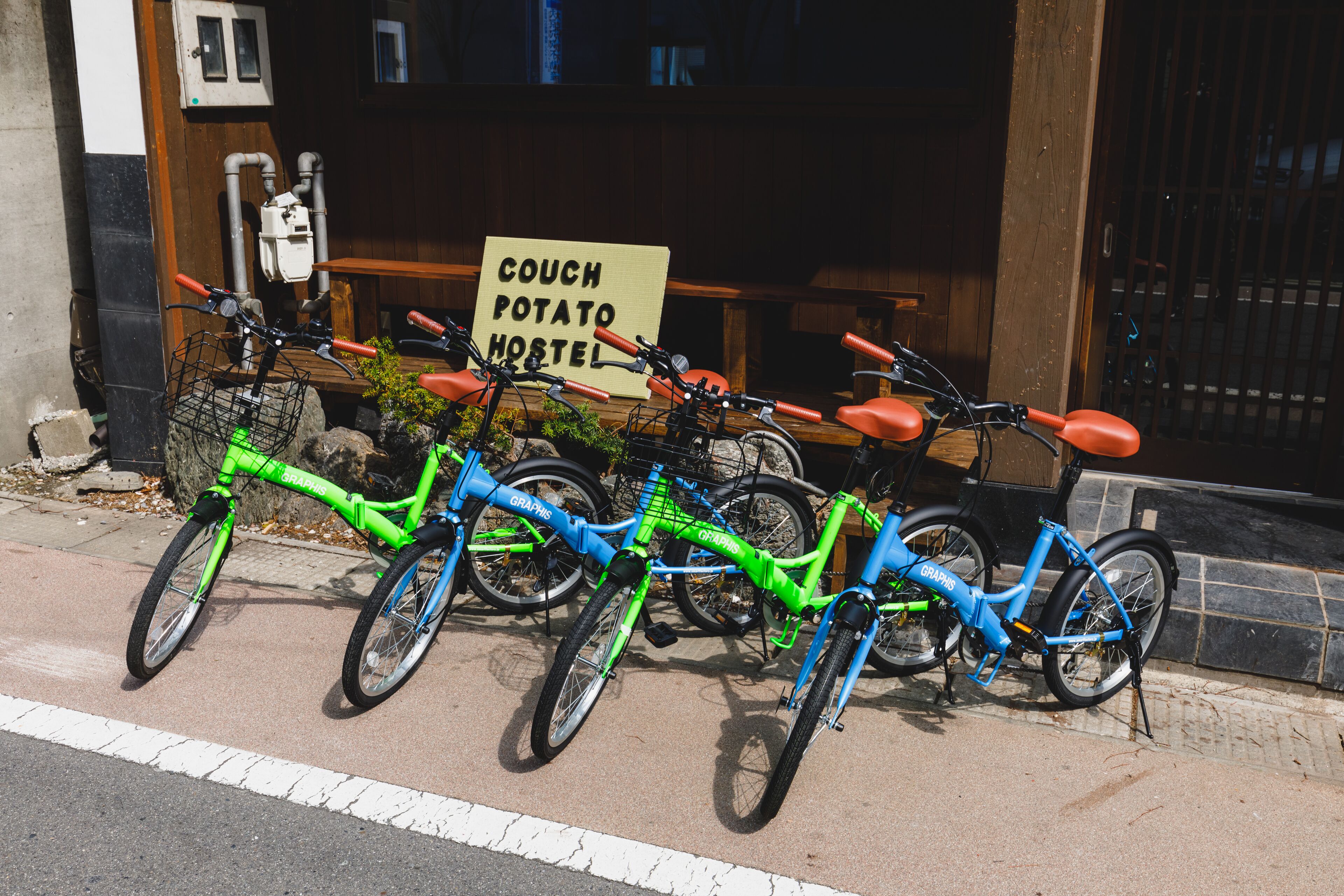A row of bicycles parked in front of a building with a sign that reads "Couch Potato Hostel".