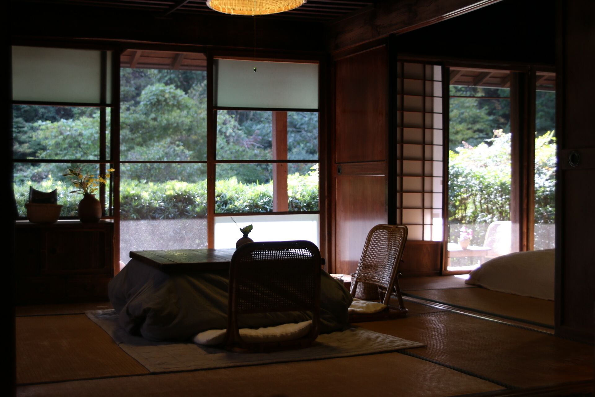 A traditional Japanese room with tatami flooring, a low table, a chair, and a sliding door leading to a garden.