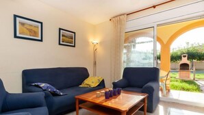 Ein Wohnzimmer mit einer Couch, Sesseln, einem Couchtisch und einer Stehlampe. An der Wand hängen zwei gerahmte Bilder.