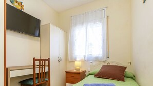 Ein Schlafzimmer mit Bett, Schreibtisch, Stuhl, Kleiderschrank und einem Fenster mit Vorhängen.