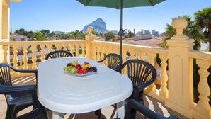 A balcony with a table set for two, a green umbrella, and a view of a mountain and cityscape. - Vacation home Gao by Interhome (Calpe/Calp)