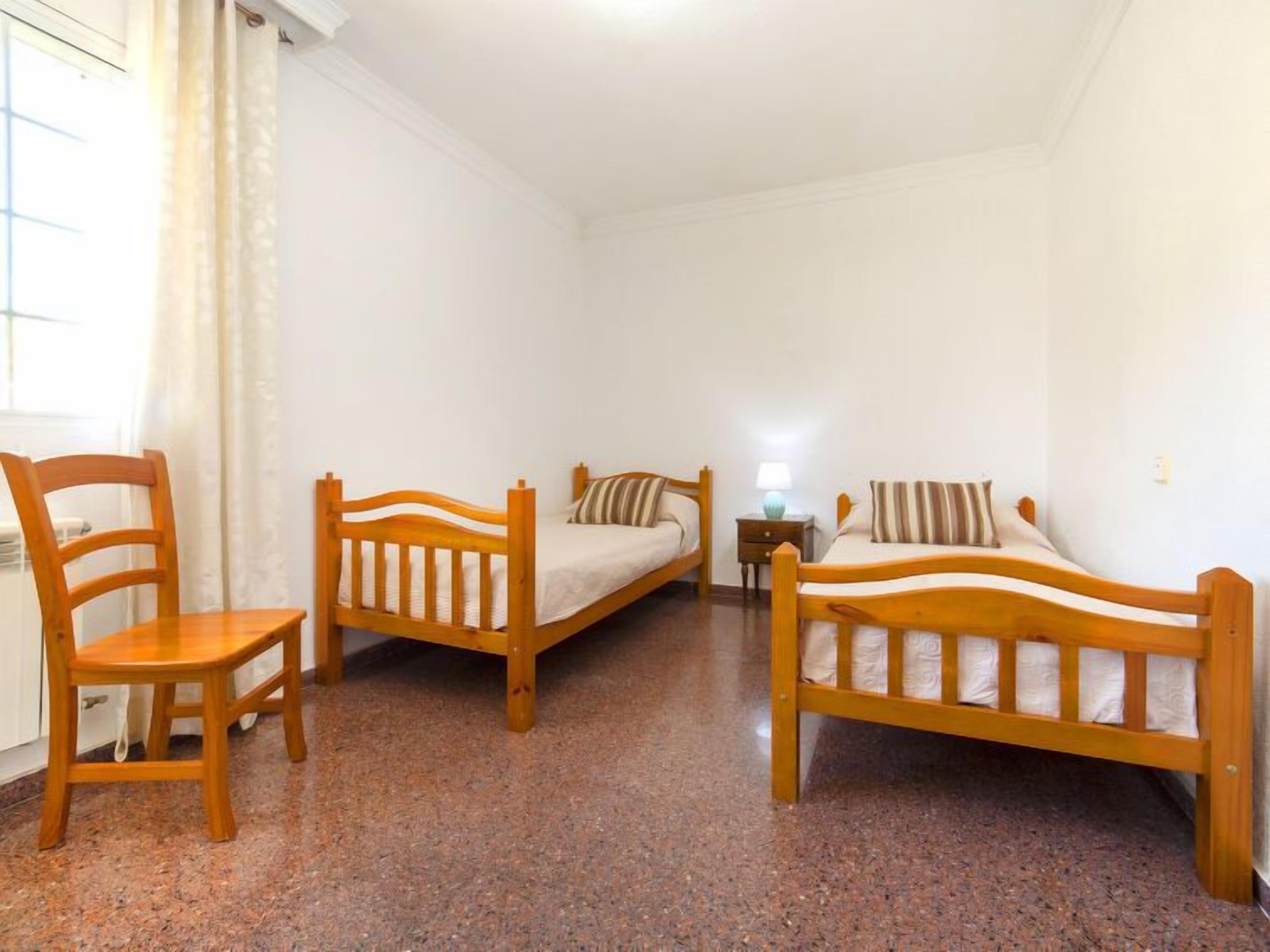 Een kamer met twee houten bedden, een houten stoel en een klein tafeltje met een lamp.