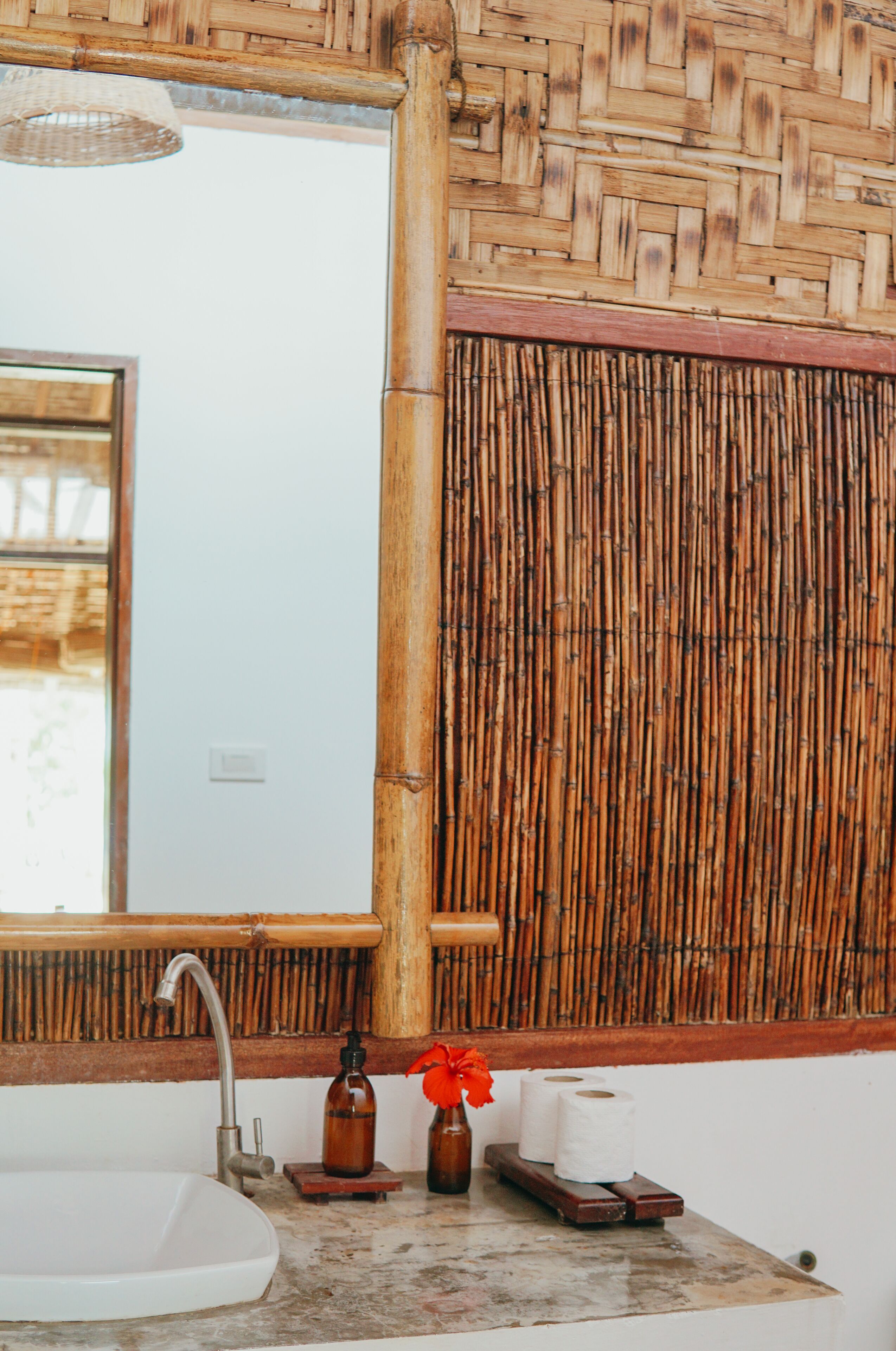 A bathroom with a white sink, a mirror, and a bamboo wall.