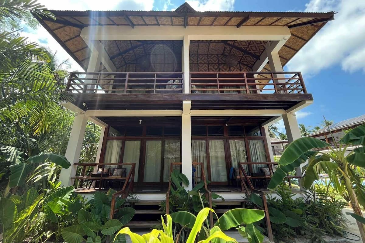 A two-story building with a balcony, surrounded by lush greenery.