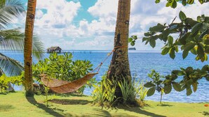 A hammock between palm trees by a calm sea with a small house in the background. - Ferra Resort Siargao (General Luna)