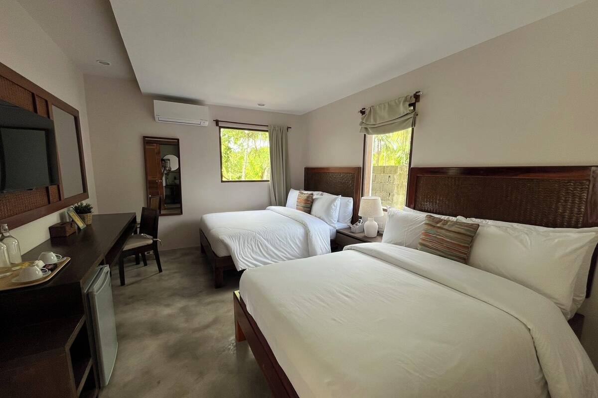 A hotel room with two beds, a desk with a chair, a television, and a window with curtains.