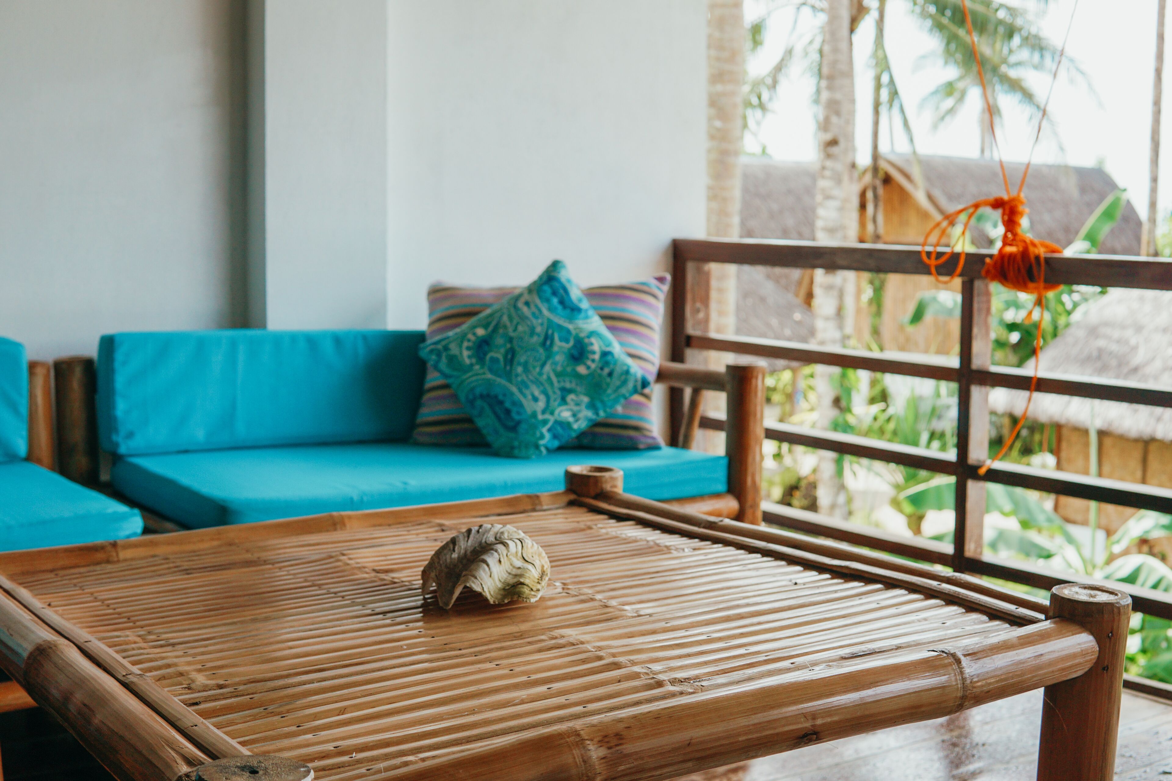 A bamboo-framed table with a decorative shell, a blue sofa with patterned cushions, and a wooden railing with a hanging ornament.
