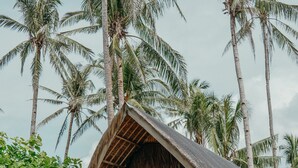 Un bungalow au toit de chaume, doté d’une véranda et entouré d’une végétation tropicale luxuriante et de palmiers.