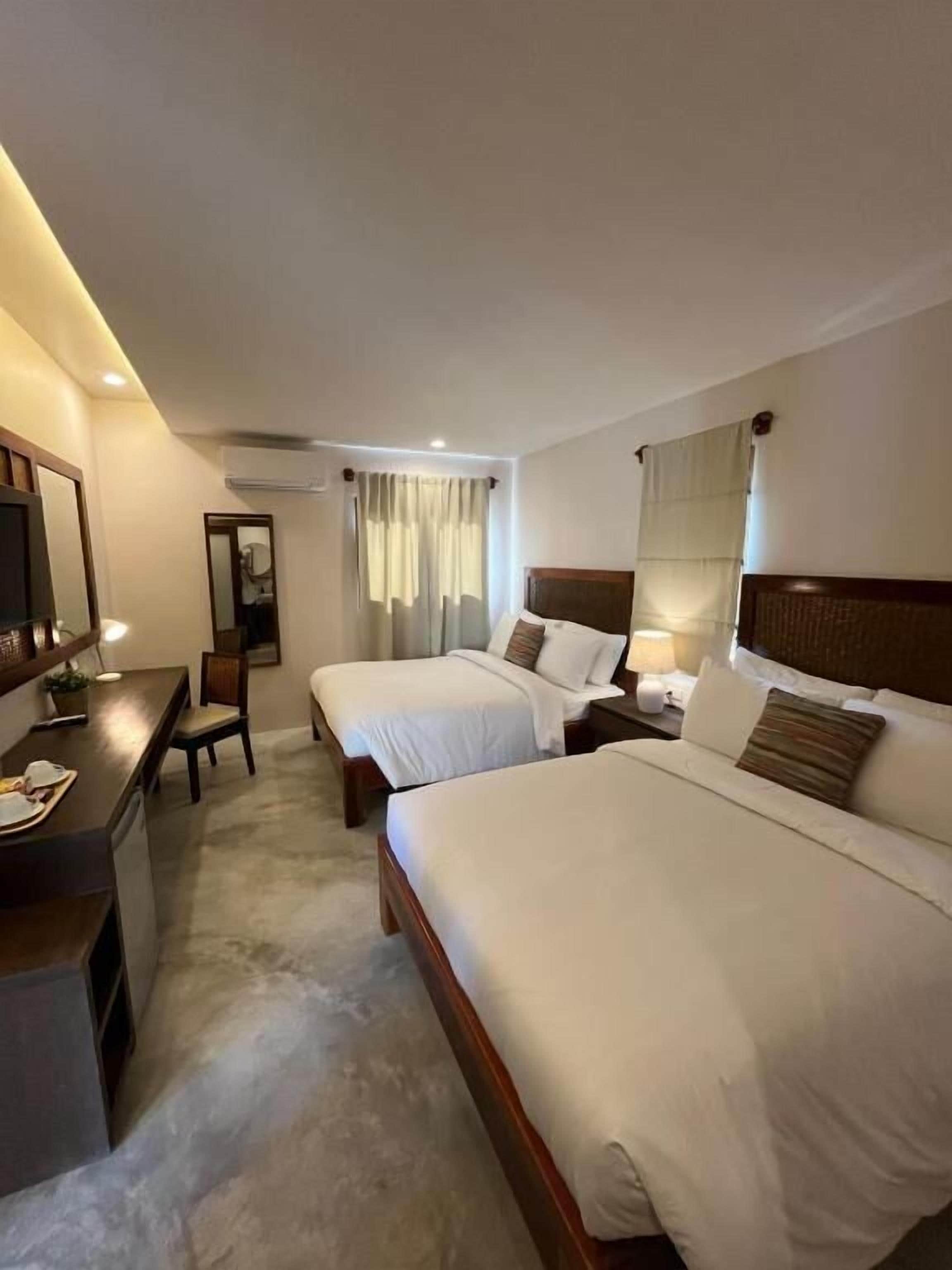 A hotel room with two beds, a desk, a chair, and a mirror.