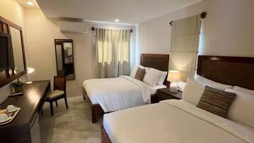 A hotel room with two beds, a desk, a chair, and a mirror.