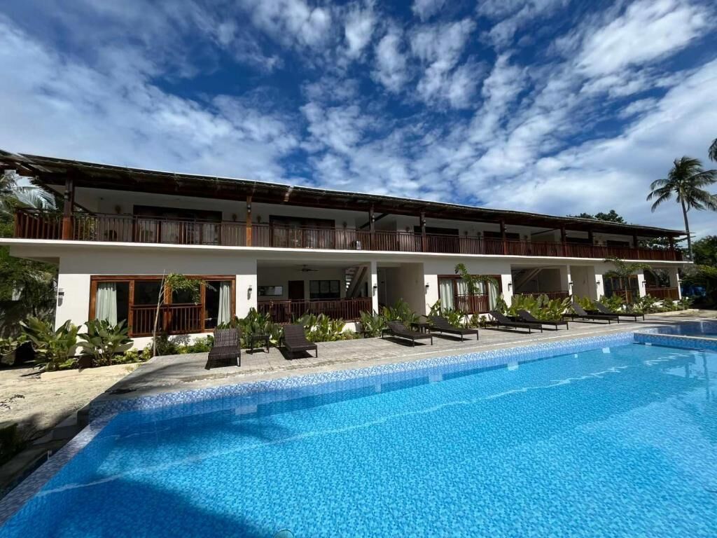 Un hotel con piscina, area esterna coperta e un edificio di due piani con balconi.