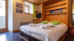 Una camera d'albergo con un letto, una televisione, scaffali in legno e una finestra vista montagne.