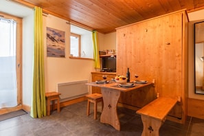 A cozy kitchen with wooden cabinets, a dining table set for two, and a window with curtains.