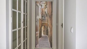 Un couloir doté d’un plancher en bois, de murs blancs et offrant une vue sur une pièce avec un mur en pierre et une porte en bois.