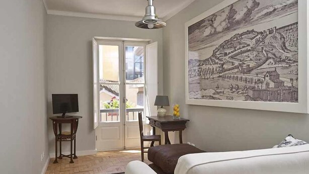 Ein Zimmer mit einer weißen Couch, einem kleinen Tisch mit Lampe, einem Fernseher auf einem Holzständer und einem großen gerahmten Kunstwerk an der Wand.