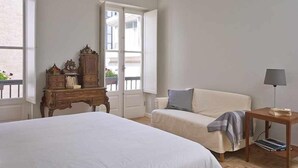 Ein Schlafzimmer mit einem großen Bett, einer Holzkommode, einem kleinen Tisch mit Lampe und einem Sofa.