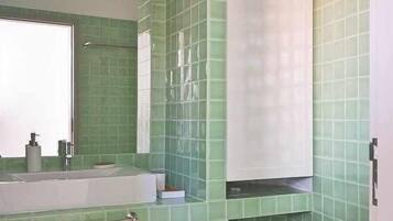 A bathroom with green tiled walls, a white sink, a toilet, and a large mirror.