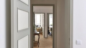 A hallway with a wooden parquet floor leading to a room with a bed and a nightstand. - Casas do Arco - Casa dos Mapas (Coimbra)