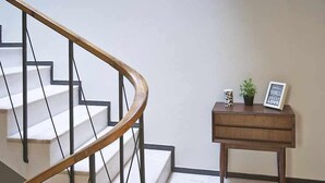A staircase with a wooden handrail and black metal balusters, leading to a landing with a small wooden table holding a framed picture and a potted plant. - Casas do Arco - Casa dos Mapas (Coimbra)