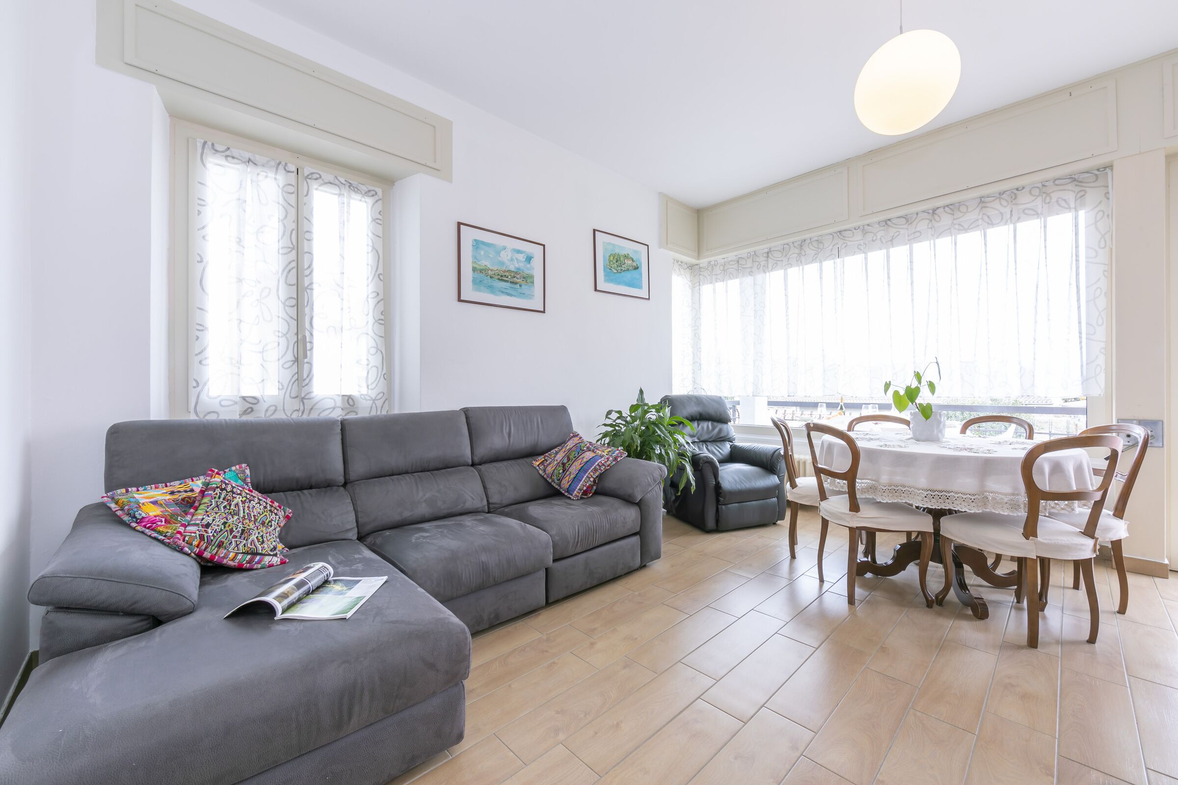 A living room with a grey sofa, a dining table with chairs, and a potted plant.