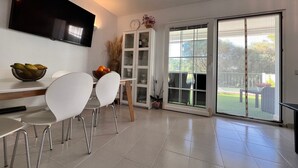 Ein moderner Essbereich mit Flachbildfernseher, einem Esstisch mit Stühlen, einem Schrank und einer Schiebetür zu einer Terrasse.