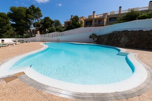 A swimming pool with a curved edge, surrounded by a white wall and a rocky slope. - Newly Renovated Apartment "Enzo" with Wi-Fi, Terrace & Pool (Son Parc)