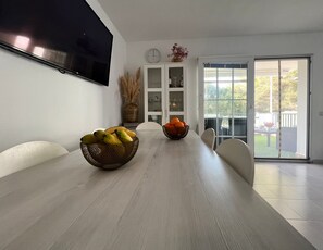 A dining area with a light-colored table, two bowls of fruit, a clock, and a sliding glass door to the outside. - Newly Renovated Apartment "Enzo" with Wi-Fi, Terrace & Pool (Son Parc)