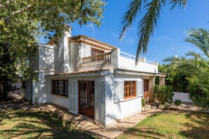 A two-story house with a balcony, a covered porch, and a small garden area. - Beautiful Villa "Beach Palmitos" with Wi-Fi, Balcony, Garden, Terraces & Pool (Can Picafort)