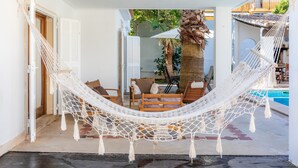 Un hamac dans un espace extérieur abrité, avec une piscine et des chaises.