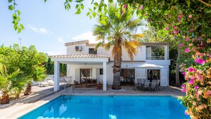 Un espace aménagé au bord de la piscine offrant une vue dégagée sur celle-ci, un coin salon couvert et un bâtiment à deux étages doté d’un balcon.