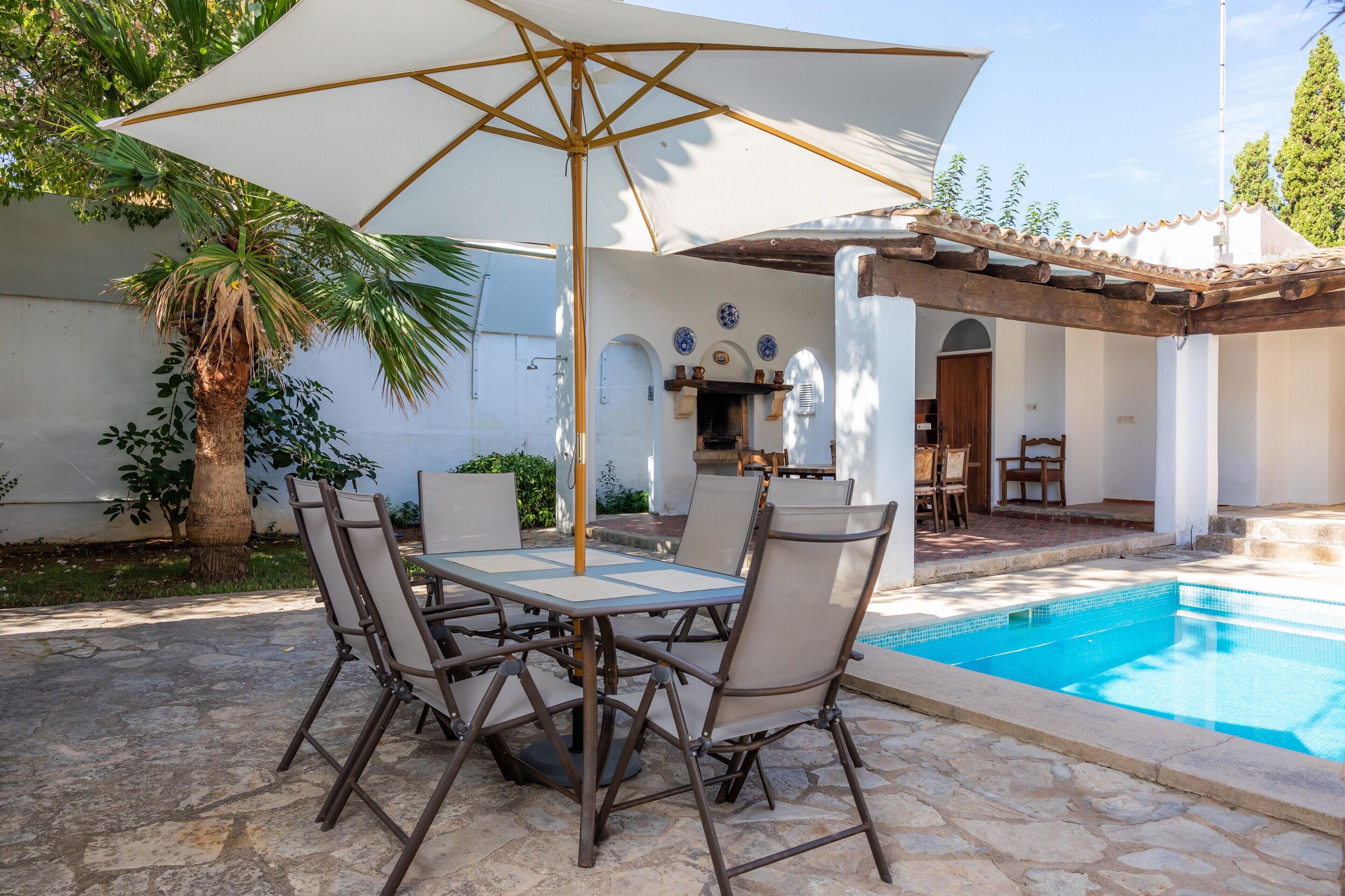An outdoor patio with a pool, a table with chairs, and a large umbrella.