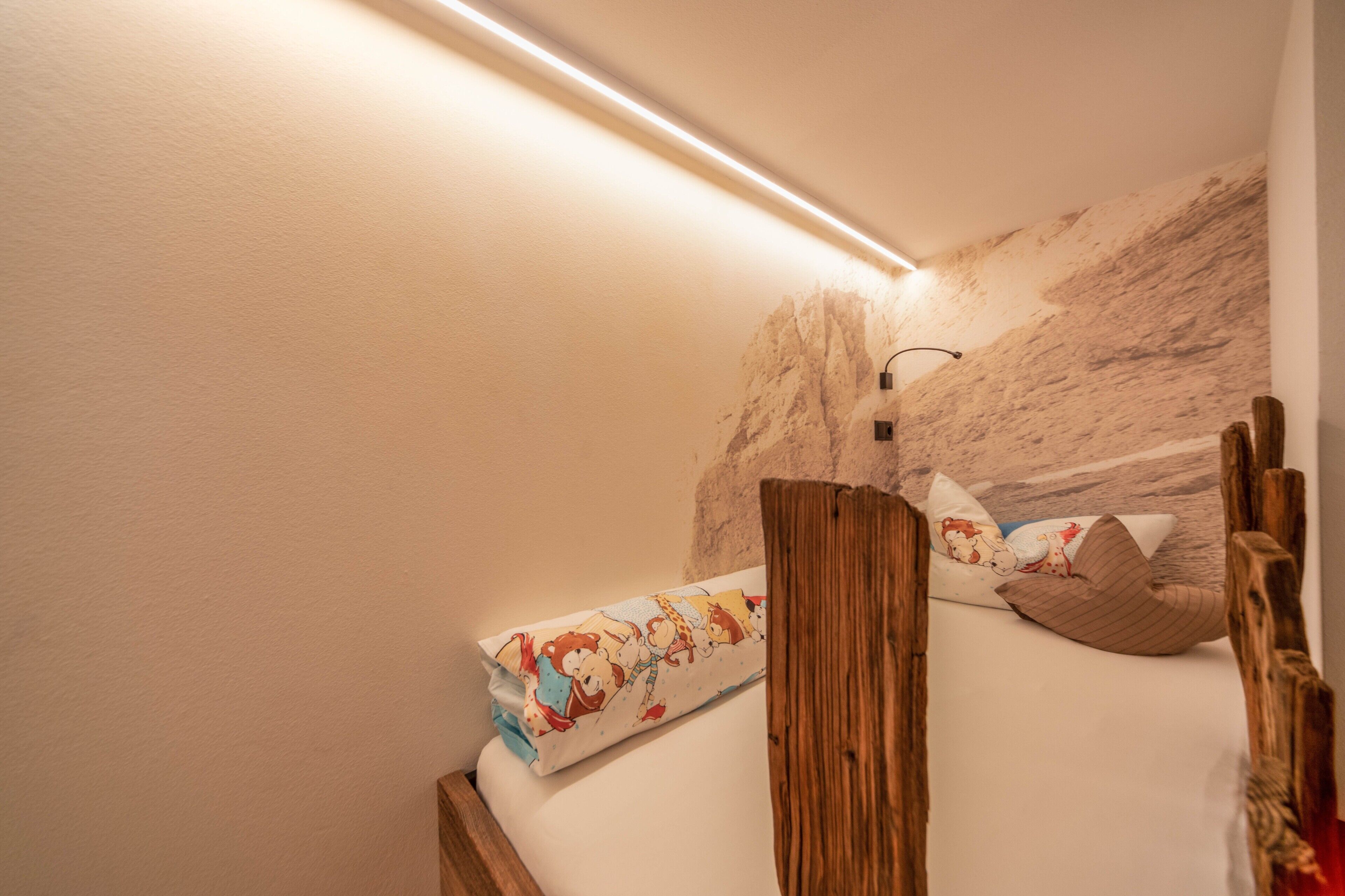 A bedroom with a wooden headboard, a bed with patterned bedding, and a wall-mounted light fixture.