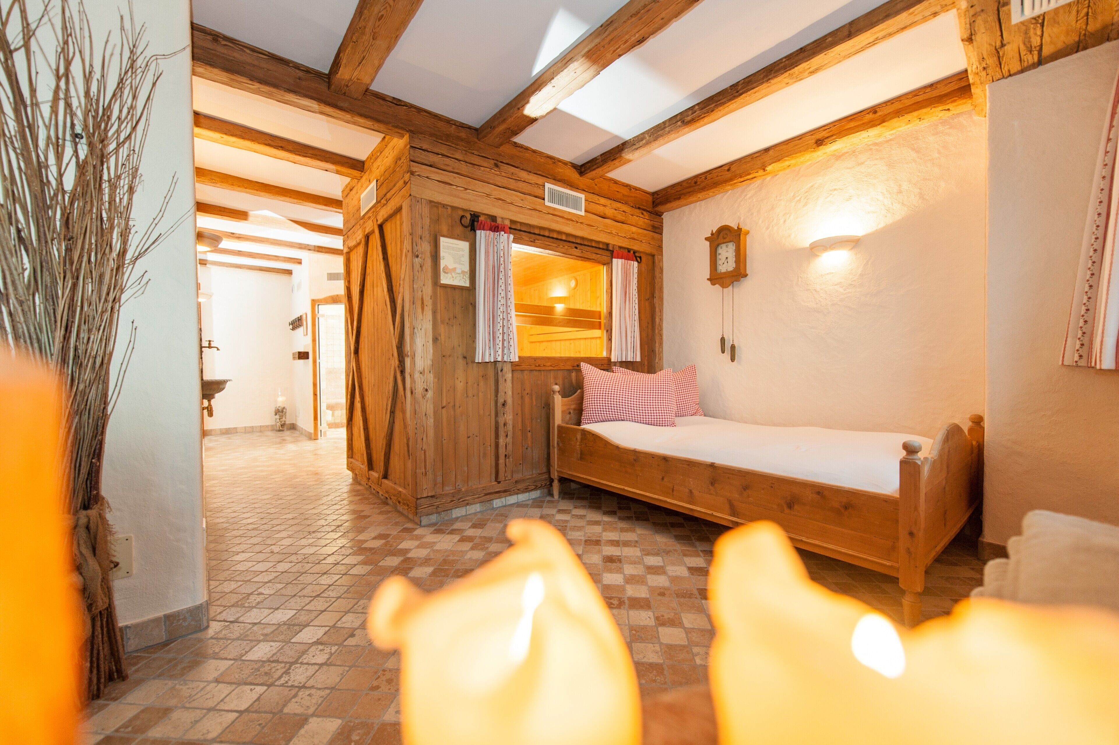 A wooden room with a bed, a wooden bench, a wall clock, and a window with curtains.