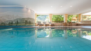 Une piscine intérieure avec vue sur les montagnes, des fauteuils confortables et une pièce baignée de lumière.
