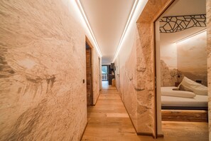 Ein Flur mit Holzboden und strukturierter Wandgestaltung, der zu einem Schlafzimmer mit Bett und Nachttisch führt.