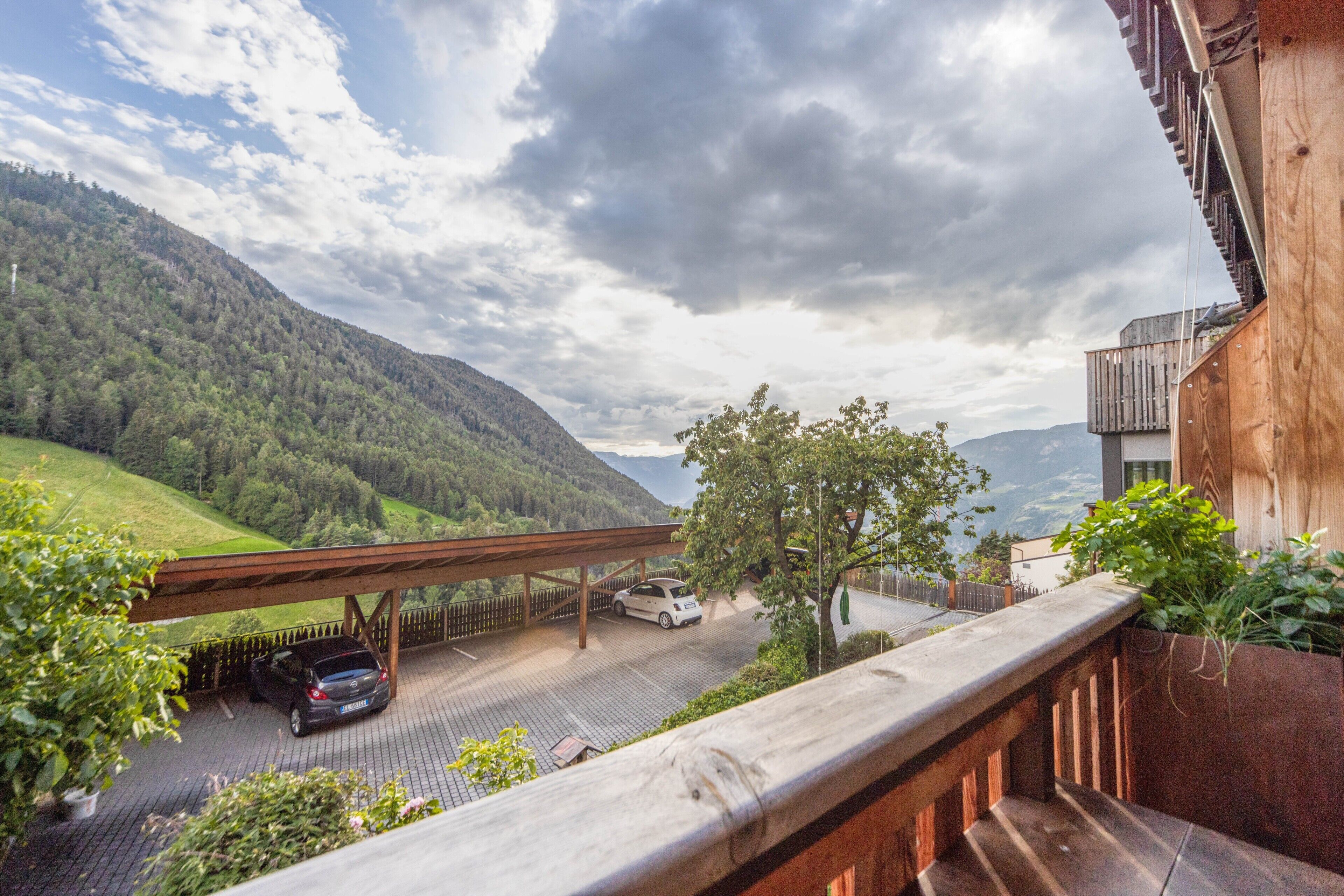 A balcony with a view of a road, a car, and a forested mountain.