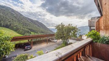 A balcony with a view of a road, a car, and a forested mountain.