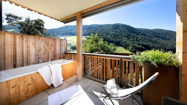 Un balcon en bois avec une baignoire, une chaise et une vue sur une chaîne de montagnes boisées.