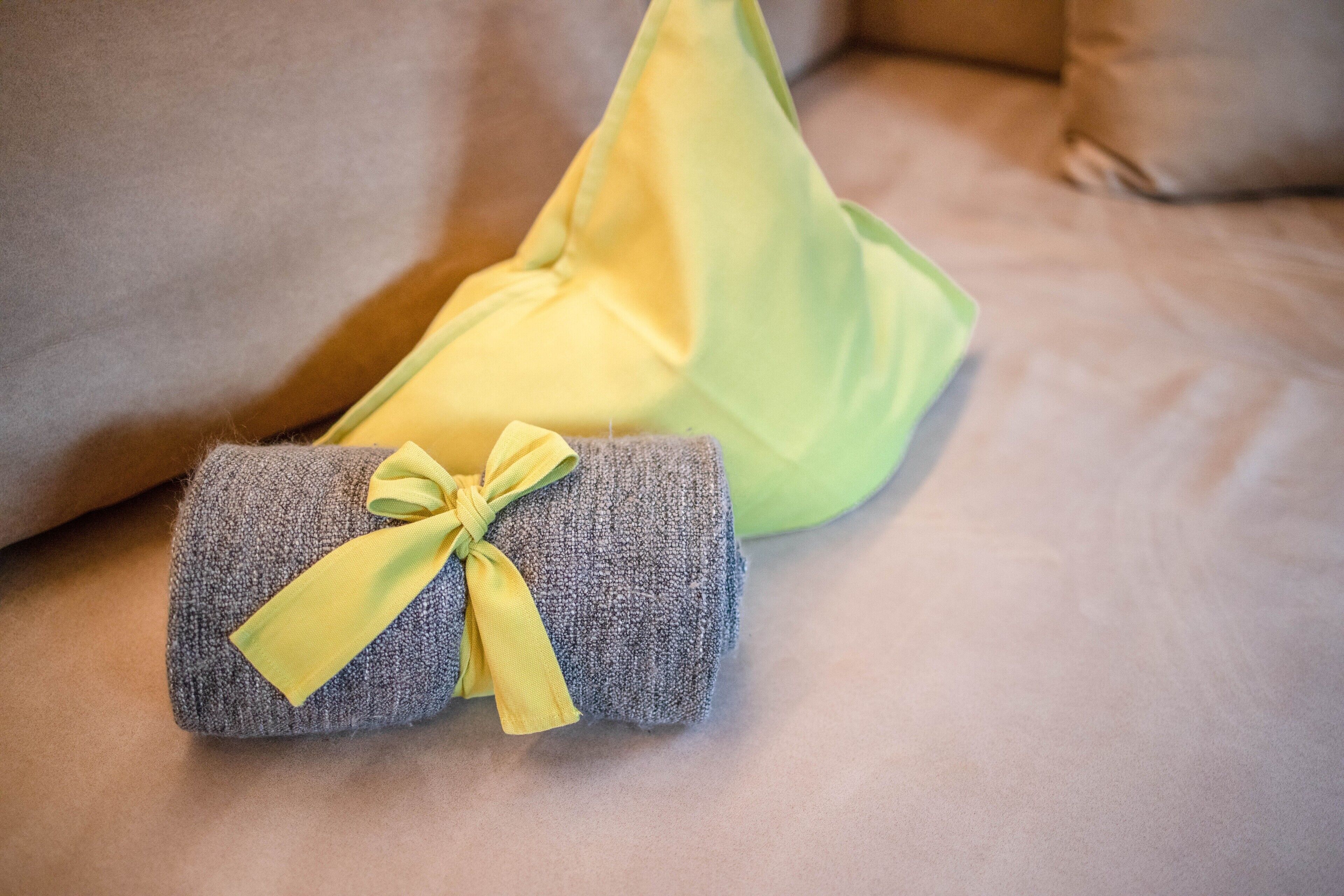 Een netjes gevouwen handdoek met een gele strik erom, op een bed met een groen kussen.