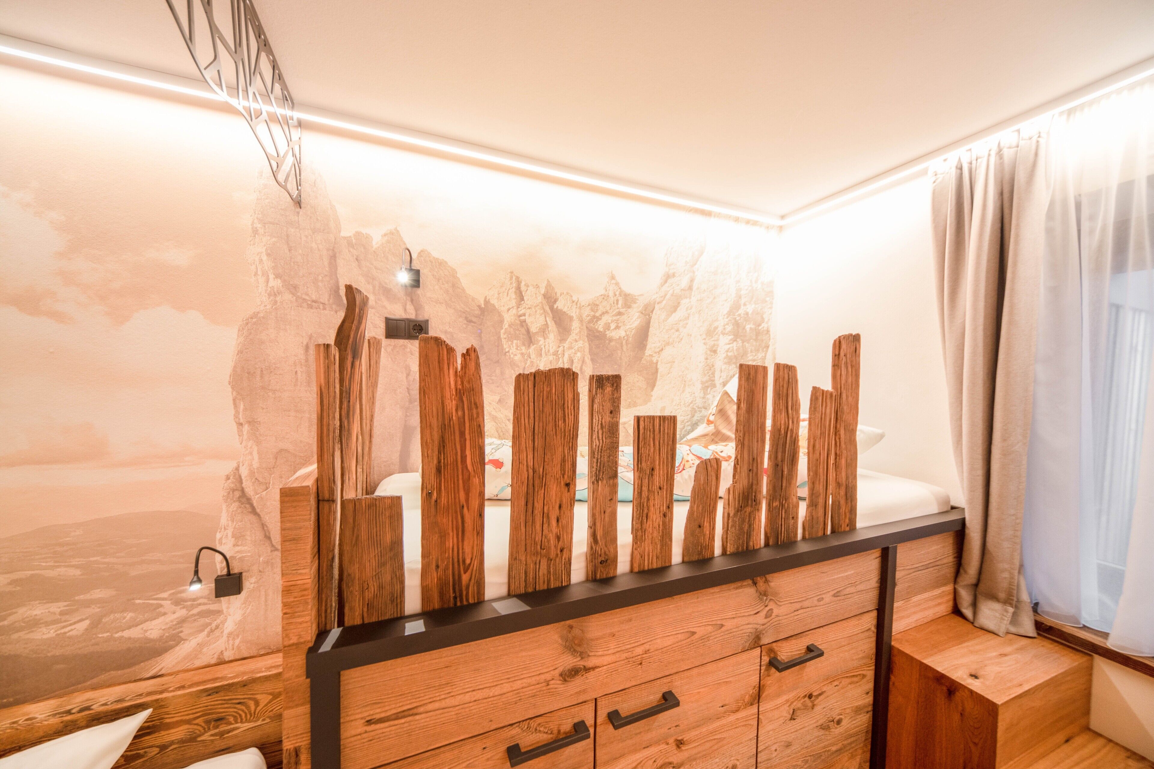 Un dormitorio con cama, cómoda de madera y un mural de paisaje montañoso en la pared.