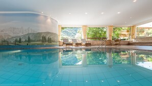 Une piscine aux carreaux bleu clair, dotée de chaises longues et ornée d’une fresque représentant des montagnes.