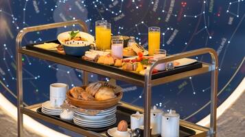 A breakfast trolley with various food items and drinks, a bowl of bread, plates, and cups, set against a starry background.