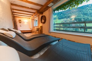 Une pièce avec un plafond en bois, un lit avec un oreiller, une chaise, une fenêtre donnant sur une forêt et une horloge murale.