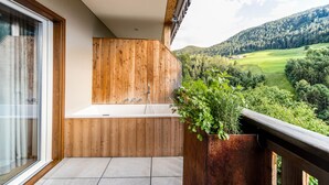 Un balcon avec une baignoire en bois, une plante en pot et une vue sur une vallée verdoyante.