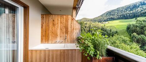 A balcony with a wooden bathtub, a potted plant, and a view of a green valley.