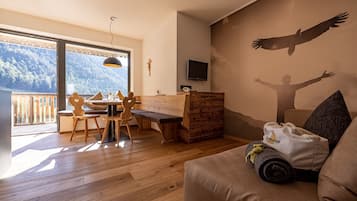Ein Zimmer mit einem Holzes Esstisch, Stühlen, einer Couch, einem Fernseher und einem Wandgemälde einer Person mit ausgebreiteten Armen.