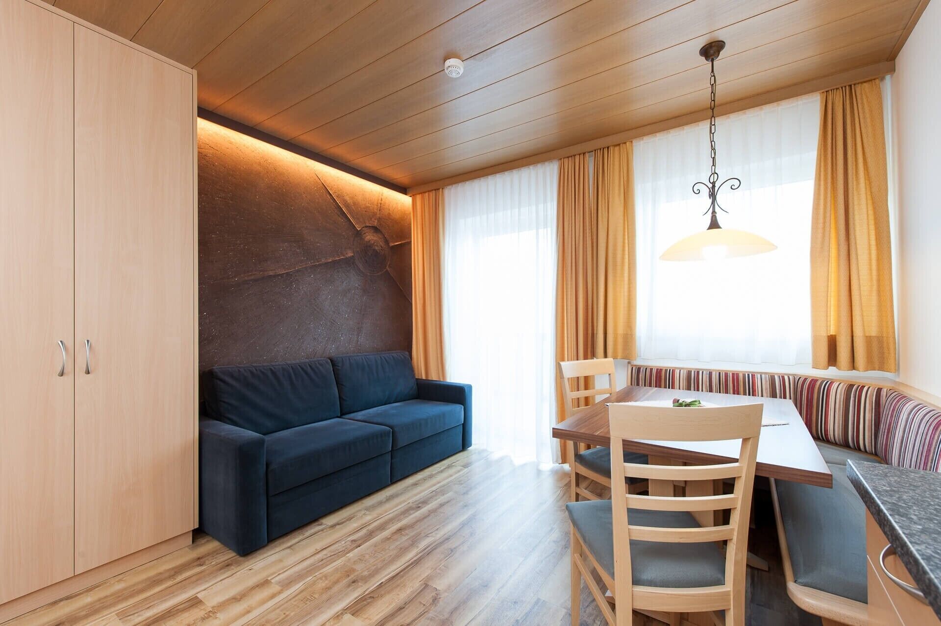 Una habitación moderna con sofá, mesa de comedor, sillas y un amplio ventanal con cortinas.